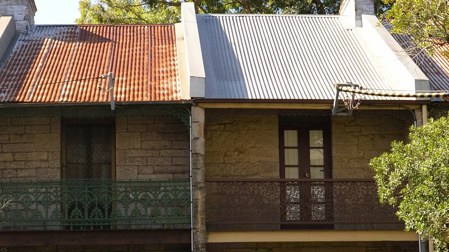 Row of attached sandstone terraces with balconies and corrugated iron roofs sharing party walls