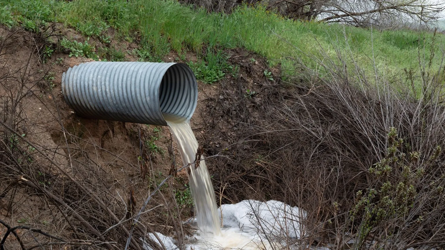 Drainage pipe discharging water through a green ravine, used to illustrate stormwater discharge and easement risk