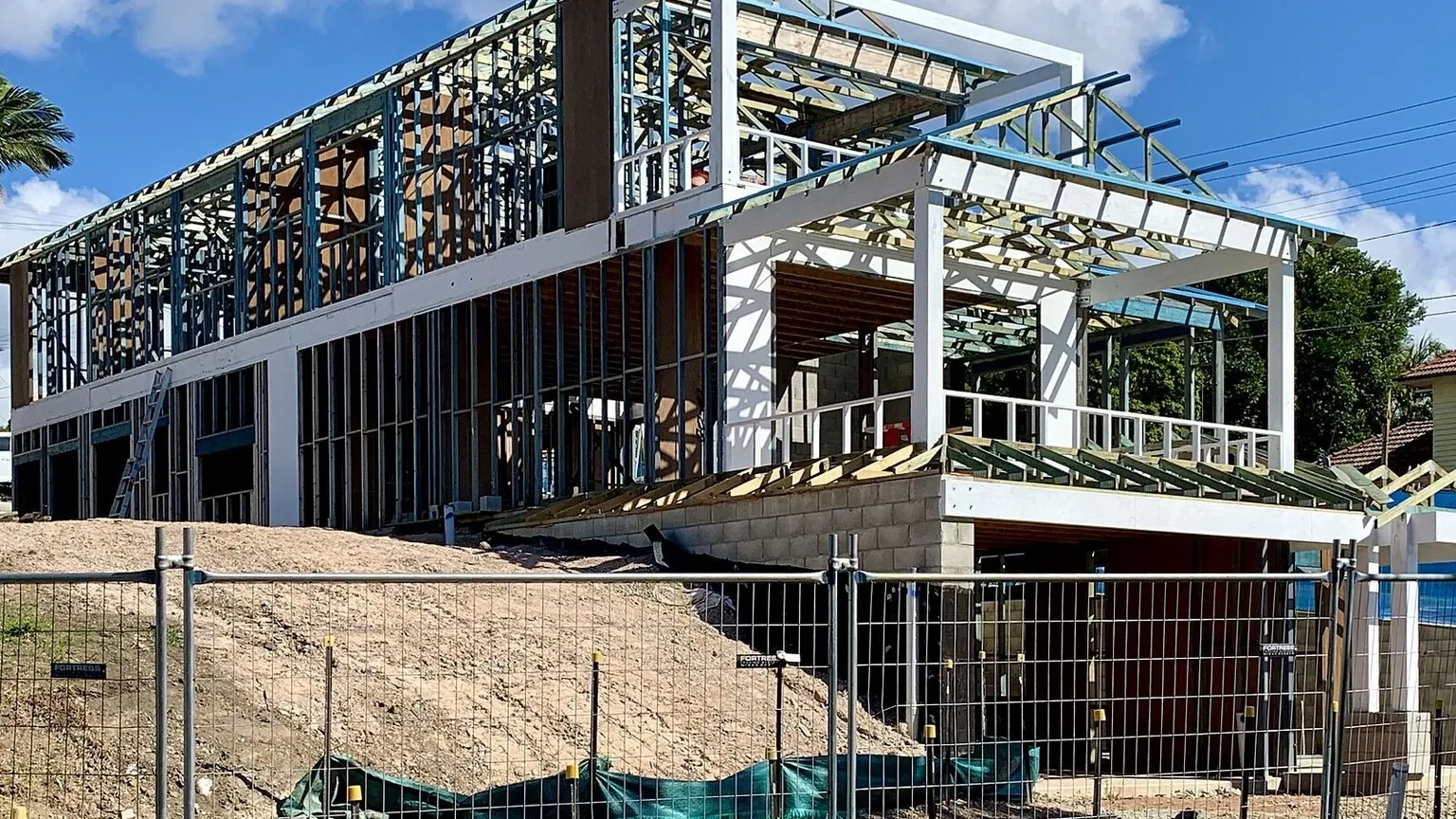 A house under construction with exposed timber wall frames, roof trusses and a concrete slab on a suburban street in Australia