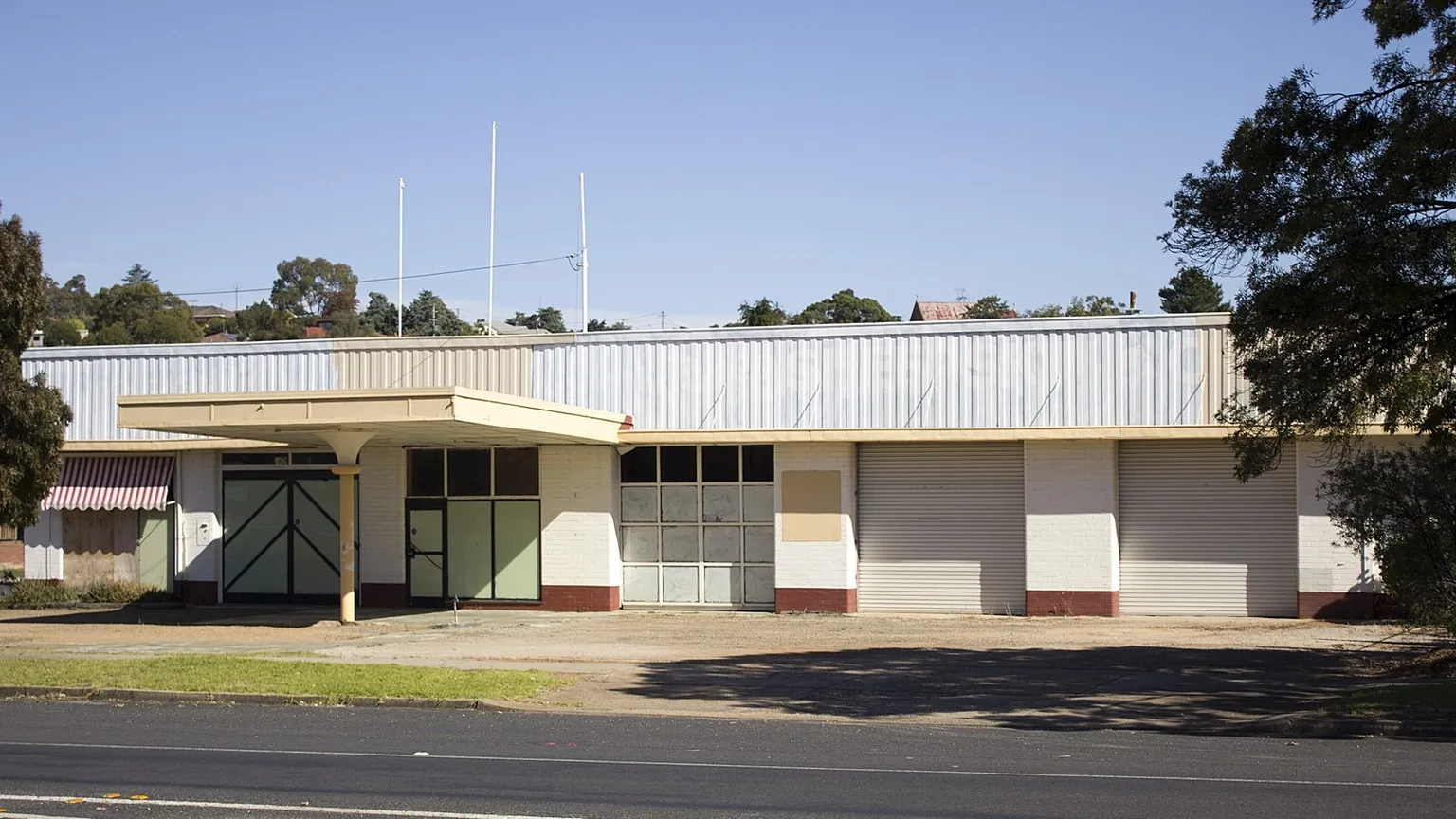 A closed former service station building with roller shutters and an empty forecourt on a country street in New South Wales