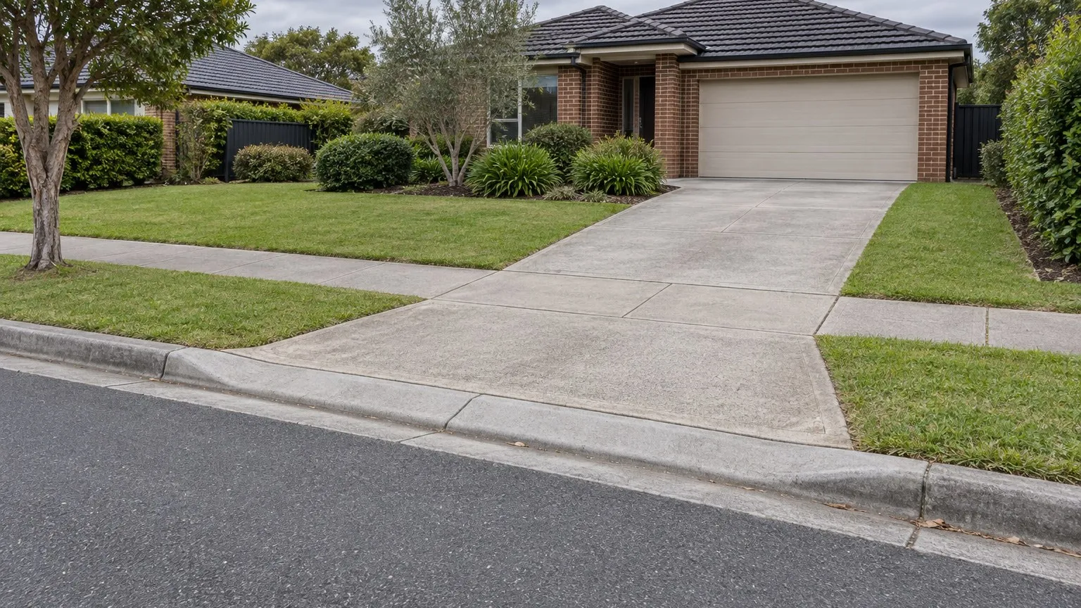 Illustrative view of a concrete driveway crossing a suburban footpath between a road and a brick house