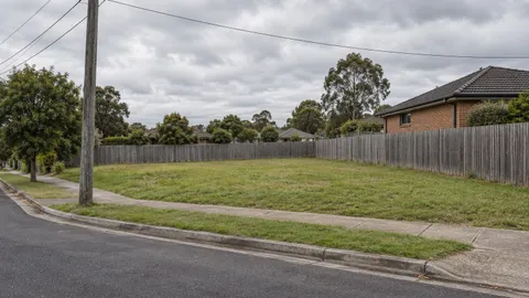 Empty grassed suburban corner lot with a street power pole at the boundary