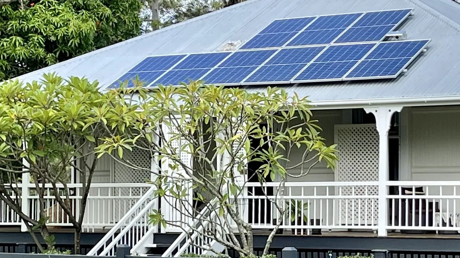 A Queenslander house with a large rooftop solar array above a white veranda in daylight