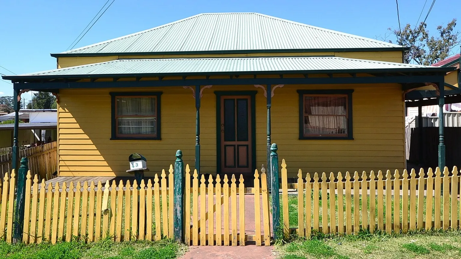 A pale weatherboard cottage with a green roof and a yellow picket fence on a suburban street in Blacktown, New South Wales