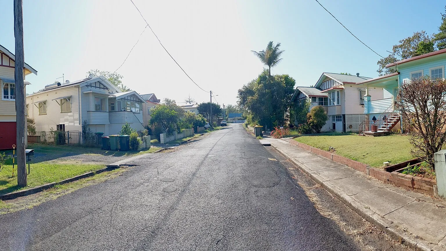 A quiet suburban residential street in northern New South Wales with low-set houses, grass verges, street trees and overhead power lines