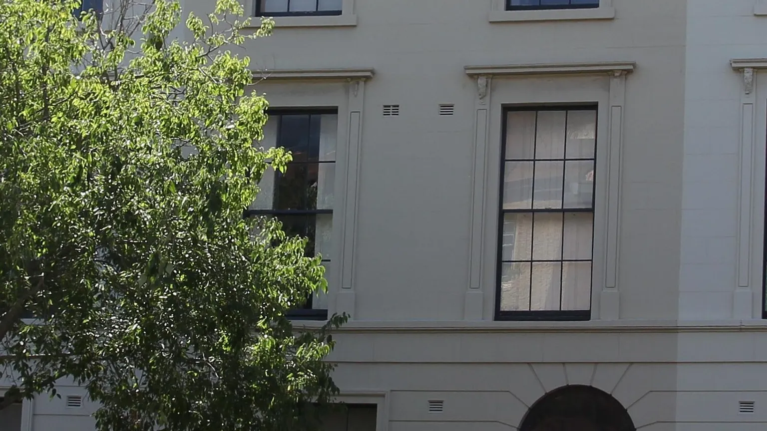 A row of attached rendered terrace houses with shared party walls and tall windows seen from the street