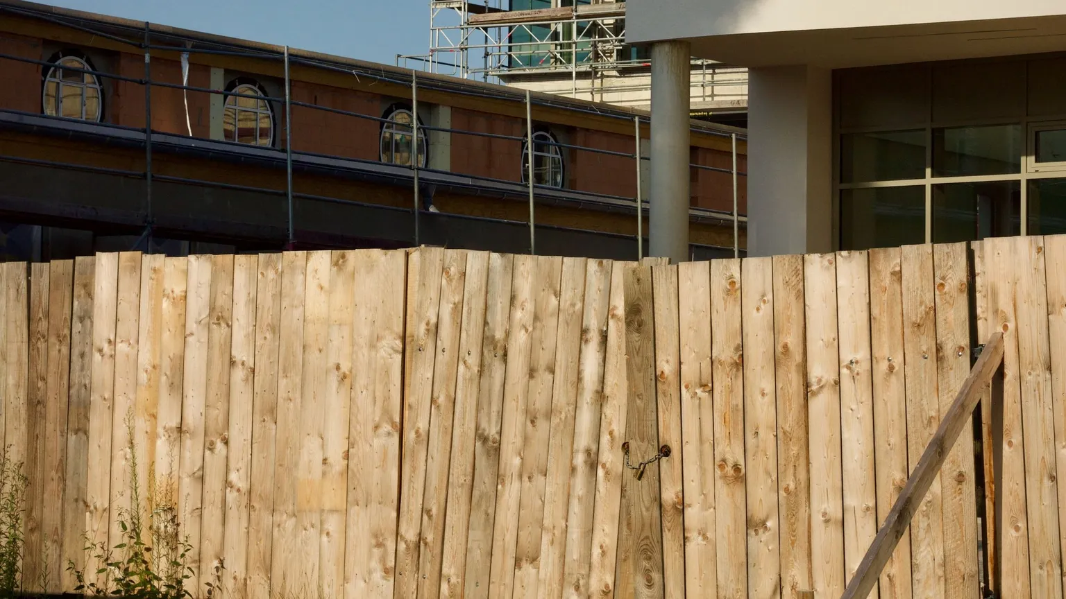 Wide view of a tall timber hoarding fence around a construction site with scaffolding and a building behind it