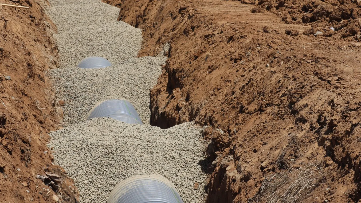 Large pipes laid in a gravel-bedded trench with excavated soil banks on either side at a services installation site