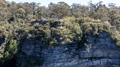 Steep bushland slope with exposed layered sandstone cliff beneath eucalypt forest.
