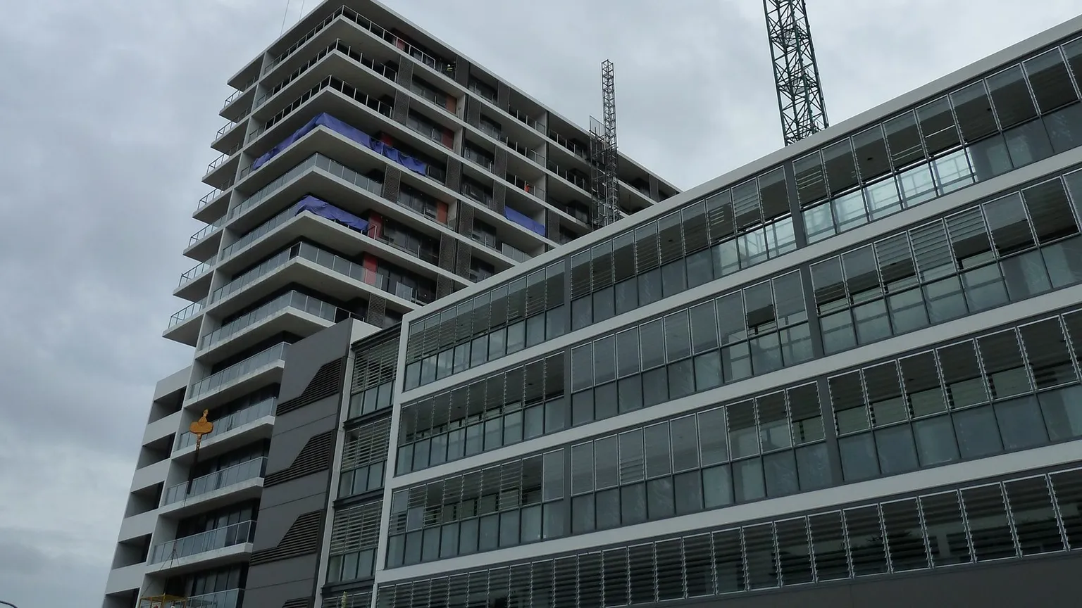 Two multi-storey apartment buildings under construction on an overcast day, showing glazed balconies, partly clad facades and scaffolding