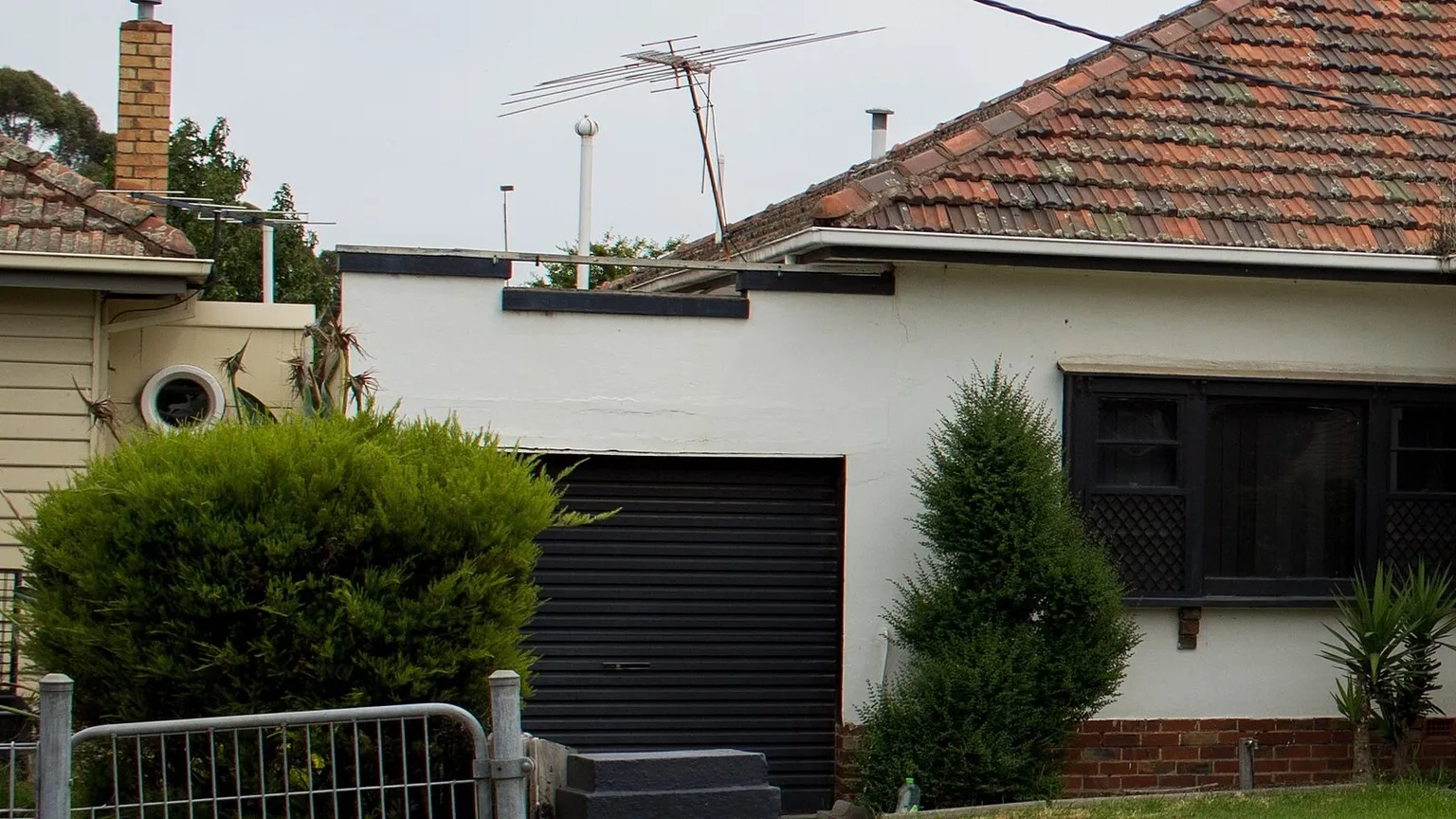 A rendered brick and stucco 1950s house with a tiled roof and a roller garage door on a suburban street in Sunshine, Victoria